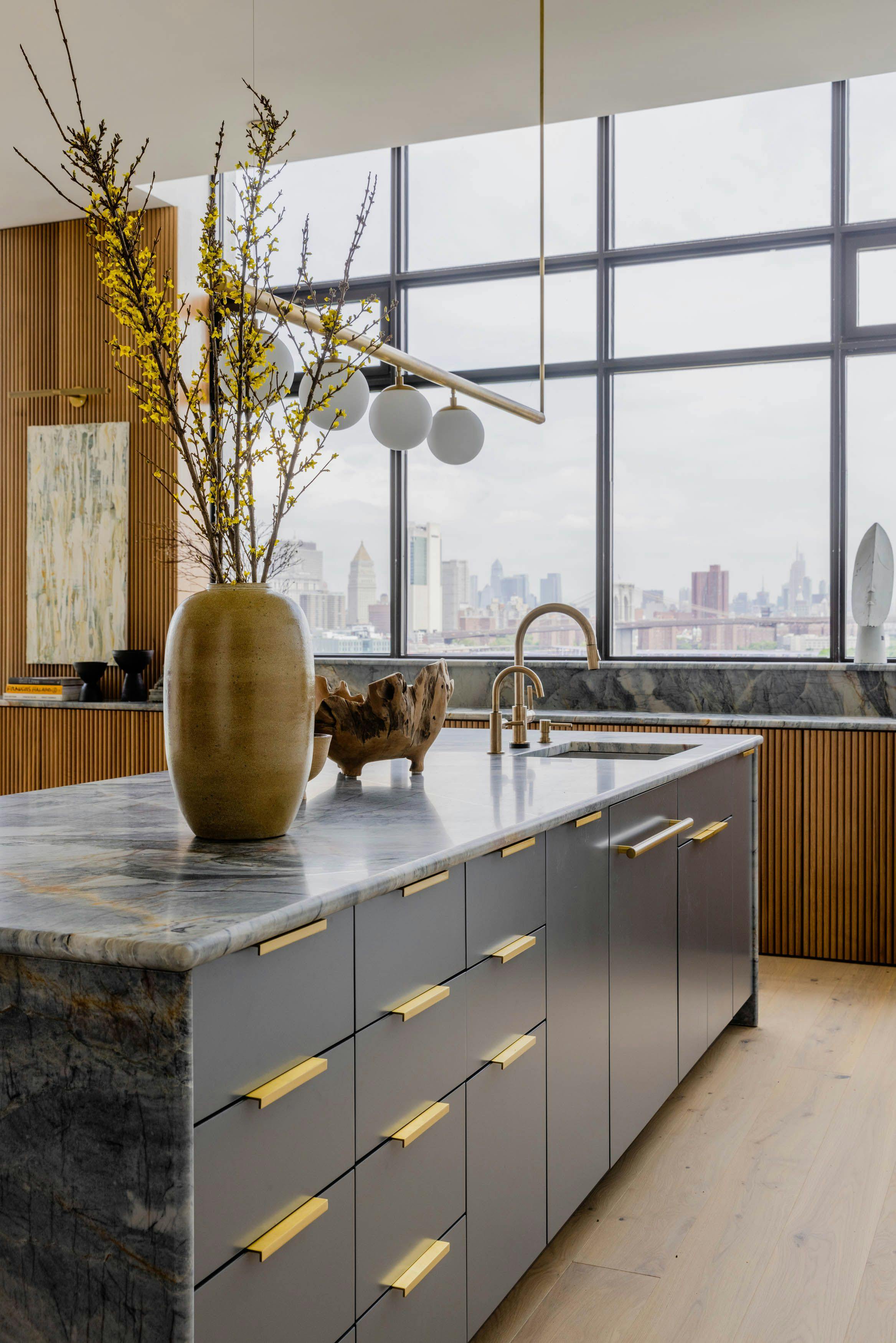A kitchen with marble counter tops and brass fixtures in The Brooklyn Bridge Kitchen, a minimalist space with warm oak millwork and a striking monolithic island.