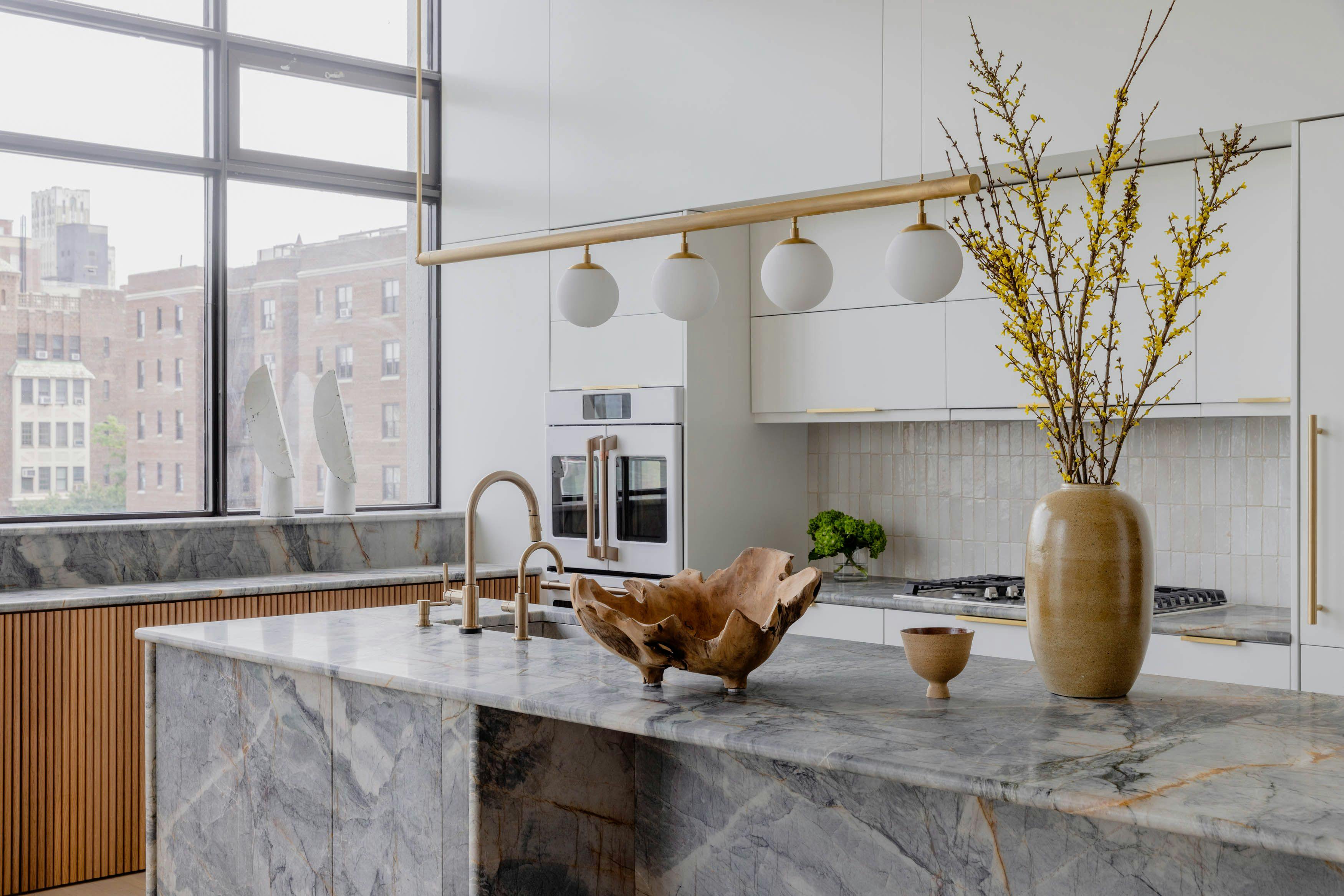A kitchen with marble countertops and a vase of flowers, set in an airy loft overlooking the Brooklyn Bridge.